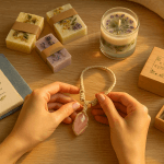 Regali fatti a mano per lei: mani che creano gioiello artigianale circondato da creazioni uniche come saponi botanici e libri rilegati a mano