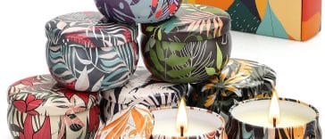 Candele di Natale profumate eleganti su tavolo decorato con pigne e rami di abete, perfette come regalo per le feste