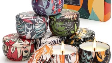 Candele di Natale profumate eleganti su tavolo decorato con pigne e rami di abete, perfette come regalo per le feste